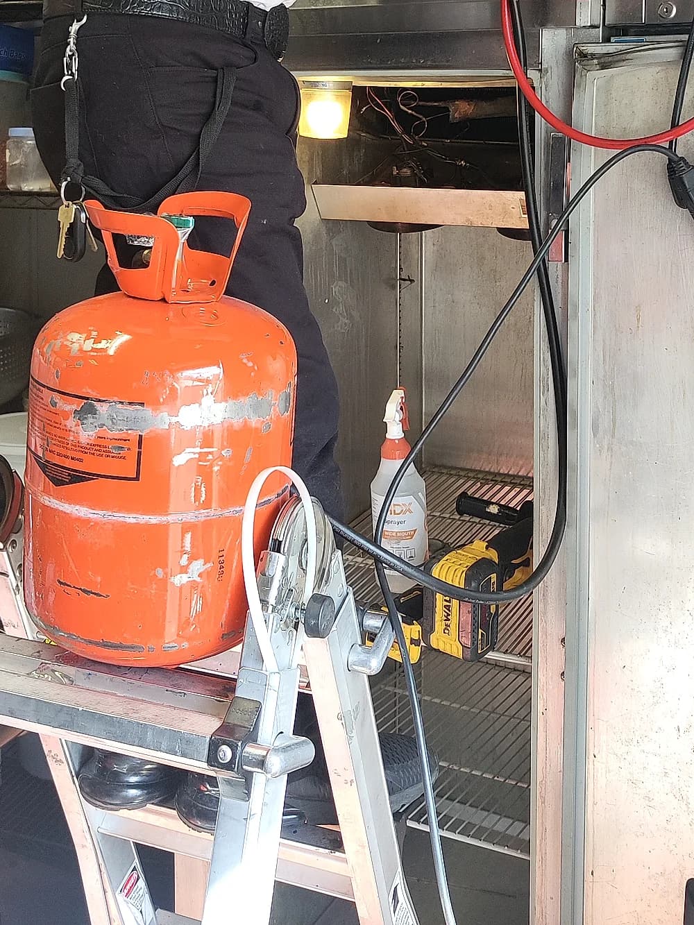 Technician using manifold gauges to service a commercial walk-in refrigeration unit