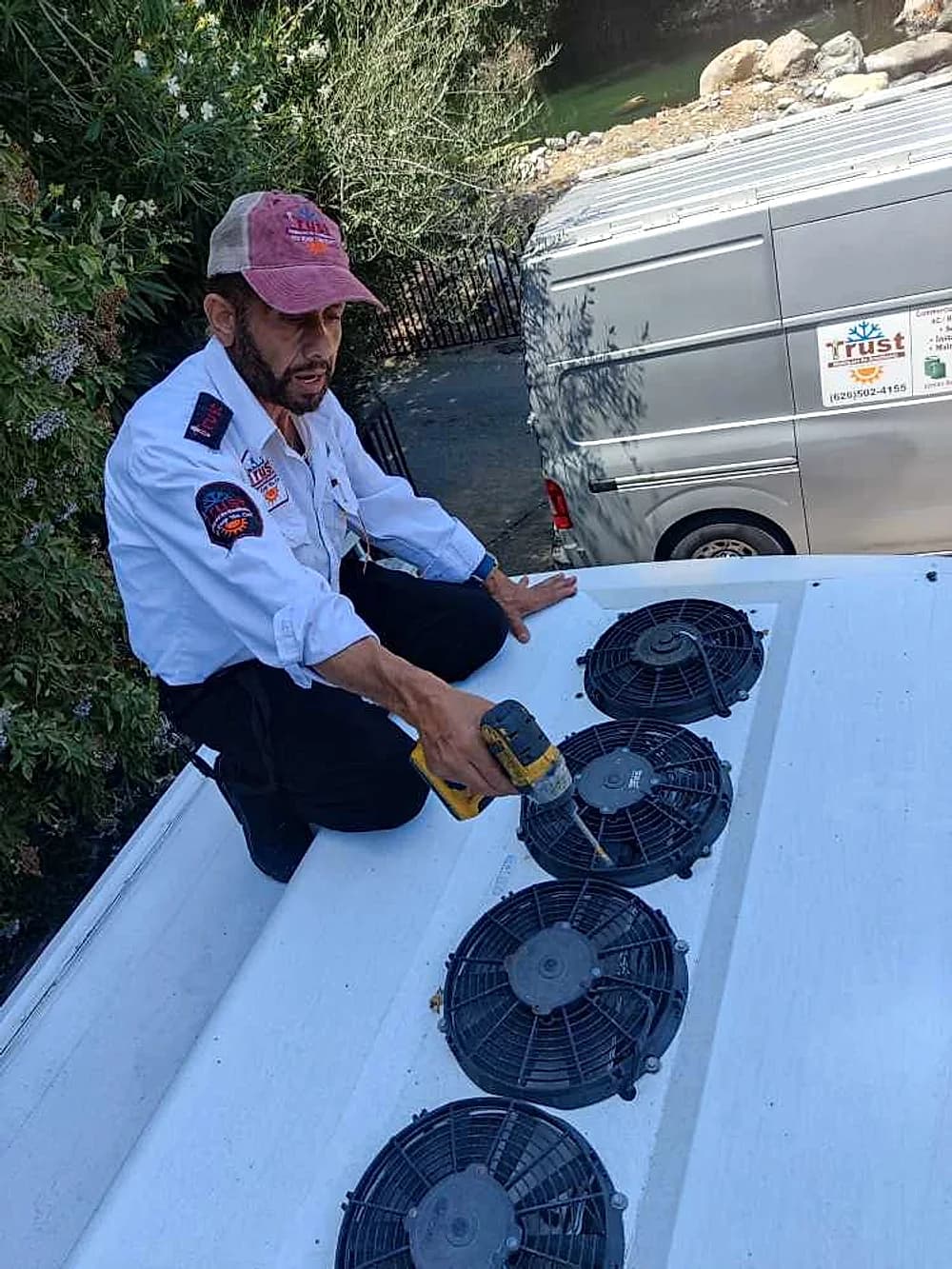 Trust Heating and Air Conditioning technician servicing condenser fans on a service van roof